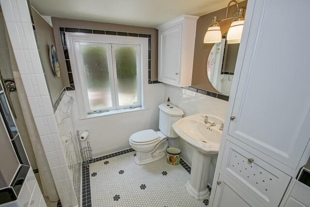 bathroom with tasteful backsplash, tile walls, toilet, and tile patterned flooring