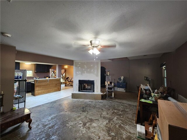 living room with ceiling fan, a textured ceiling, and a fireplace