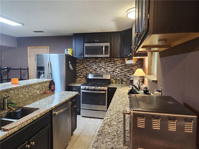 kitchen with light tile patterned flooring, sink, tasteful backsplash, appliances with stainless steel finishes, and light stone countertops