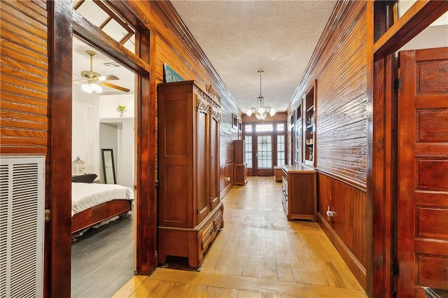 corridor featuring french doors, a textured ceiling, an inviting chandelier, crown molding, and light hardwood / wood-style flooring