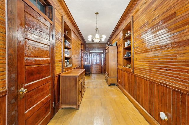 corridor with a notable chandelier, wood walls, built in shelves, and light hardwood / wood-style floors