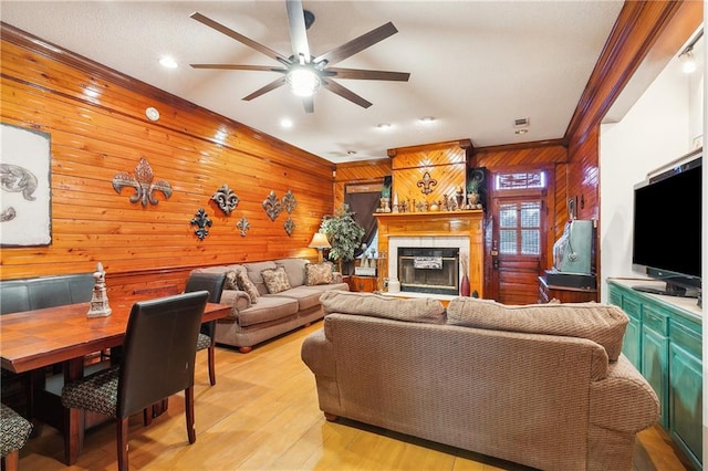 living room with light wood-type flooring, ceiling fan, wood walls, ornamental molding, and a fireplace