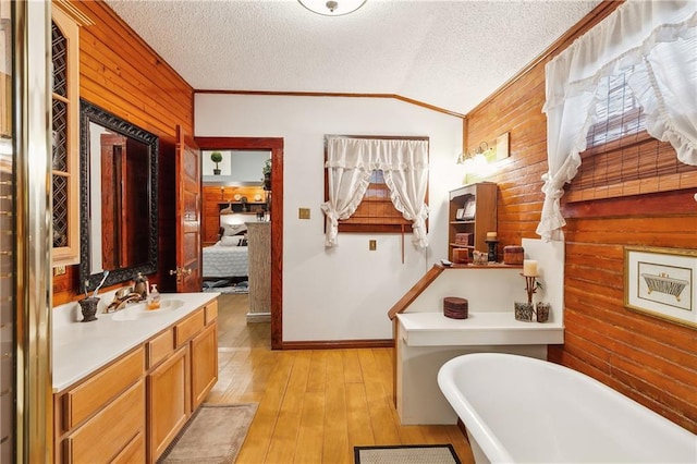 bathroom featuring a bath, vanity, vaulted ceiling, hardwood / wood-style floors, and wood walls