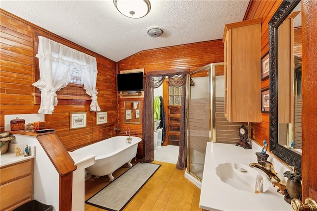 bathroom with wood walls, hardwood / wood-style floors, vaulted ceiling, and sink