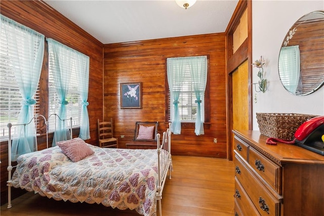 bedroom featuring wood walls, light wood-type flooring, and multiple windows