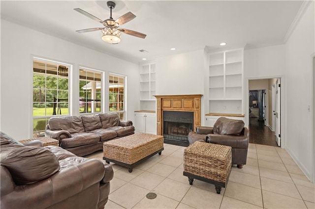 living room with built in shelves, light tile patterned floors, ceiling fan, and crown molding