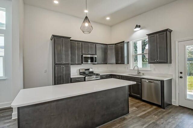 kitchen with dark wood-type flooring, pendant lighting, a center island, stainless steel appliances, and sink