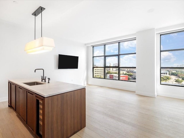 kitchen with a center island with sink, sink, wine cooler, light hardwood / wood-style flooring, and decorative light fixtures