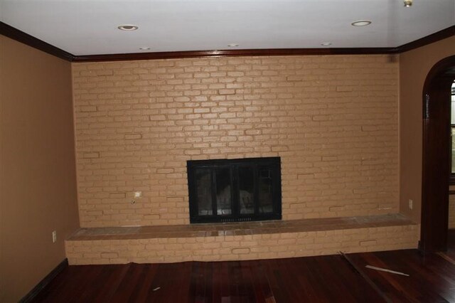 unfurnished living room featuring hardwood / wood-style floors, a brick fireplace, ornamental molding, and brick wall