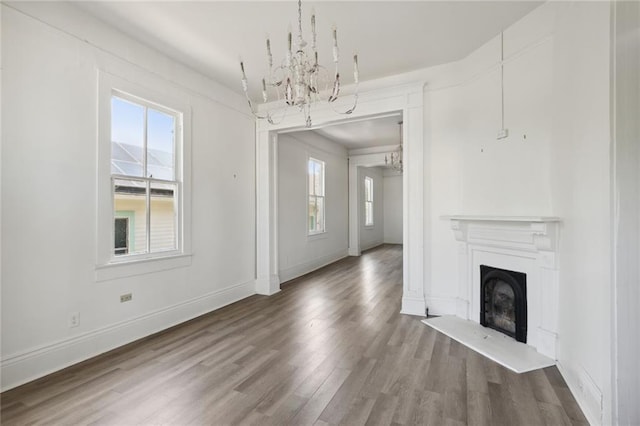 unfurnished living room featuring a notable chandelier, a fireplace, baseboards, and wood finished floors