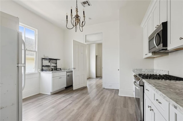 kitchen featuring appliances with stainless steel finishes, light hardwood / wood-style floors, white cabinets, and a chandelier