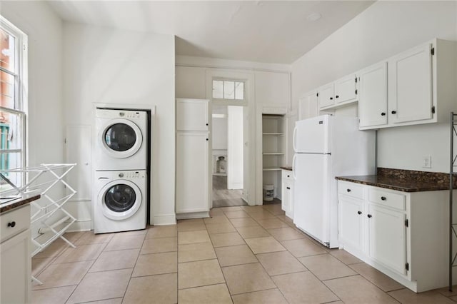 kitchen featuring white cabinets, white refrigerator, stacked washing maching and dryer, and light tile patterned flooring