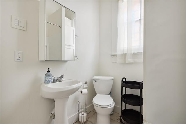 half bath with toilet, baseboards, a sink, and tile patterned floors