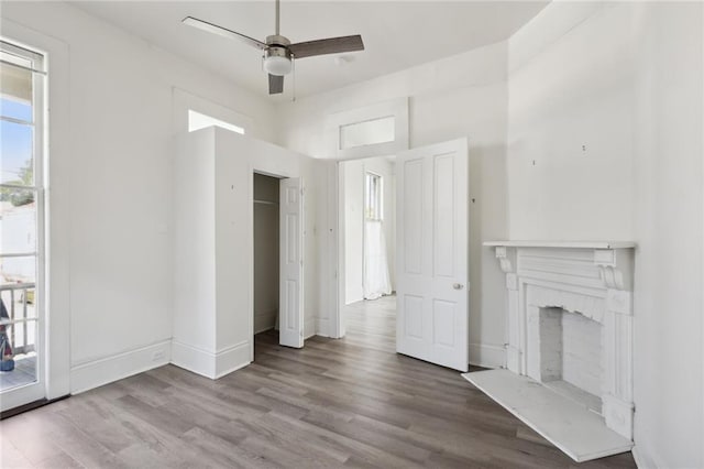 unfurnished living room with a ceiling fan, a fireplace, baseboards, and wood finished floors