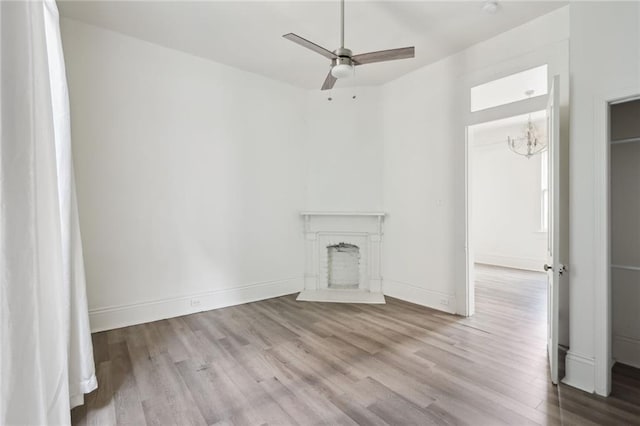 unfurnished living room featuring a fireplace with raised hearth, ceiling fan, wood finished floors, and baseboards