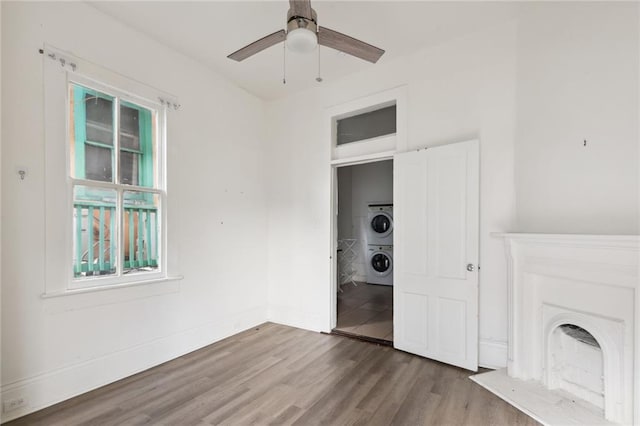 unfurnished bedroom featuring baseboards, a ceiling fan, wood finished floors, stacked washing maching and dryer, and a fireplace