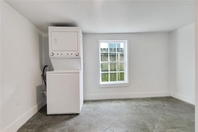 clothes washing area with baseboards and stacked washer and clothes dryer