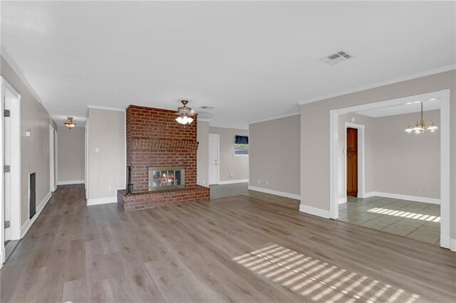 unfurnished living room featuring ceiling fan with notable chandelier, a brick fireplace, wood-type flooring, ornamental molding, and brick wall