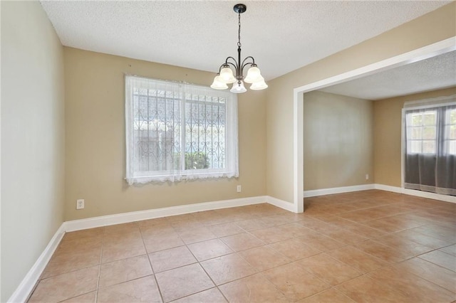 empty room with light tile patterned floors, a textured ceiling, and a chandelier