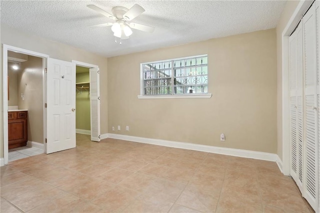 unfurnished bedroom featuring ceiling fan, connected bathroom, a textured ceiling, and light tile patterned floors