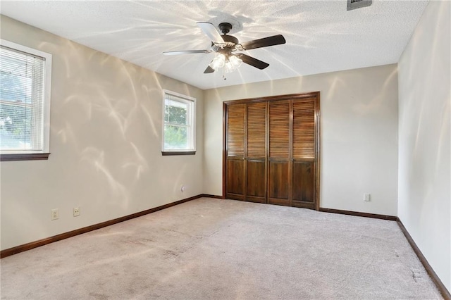 unfurnished bedroom featuring ceiling fan, light colored carpet, a textured ceiling, and a closet