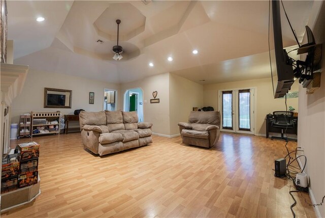 living room featuring ceiling fan, french doors, light wood-type flooring, and a raised ceiling