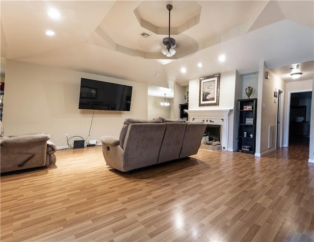 living room with ceiling fan, a raised ceiling, and light wood-type flooring