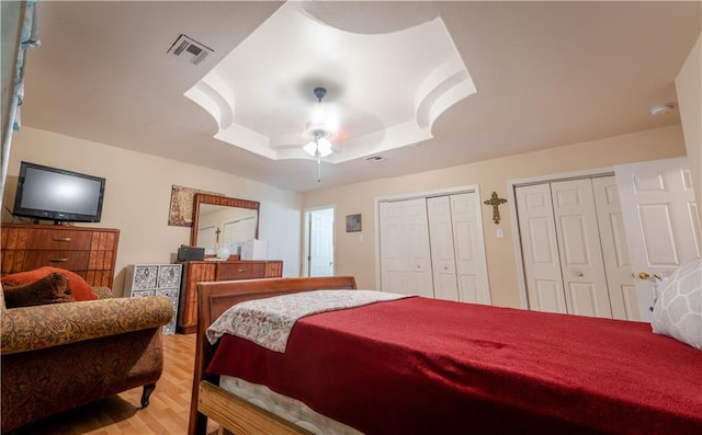 bedroom featuring ceiling fan, light hardwood / wood-style flooring, a raised ceiling, and multiple closets