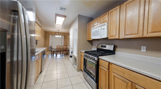 kitchen with light tile patterned floors, appliances with stainless steel finishes, a notable chandelier, light brown cabinets, and decorative light fixtures