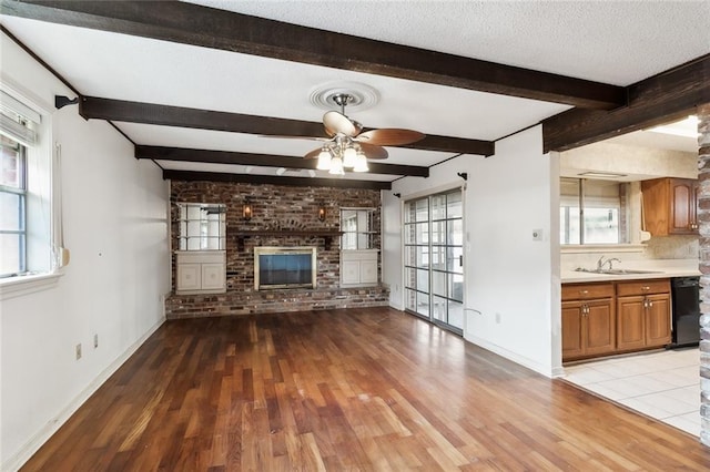 unfurnished living room featuring a textured ceiling, light tile patterned floors, a brick fireplace, ceiling fan, and brick wall