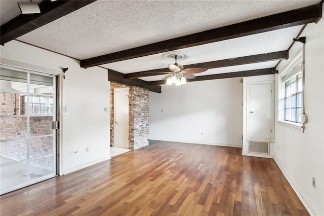 unfurnished room featuring a textured ceiling, hardwood / wood-style floors, ceiling fan, brick wall, and beamed ceiling