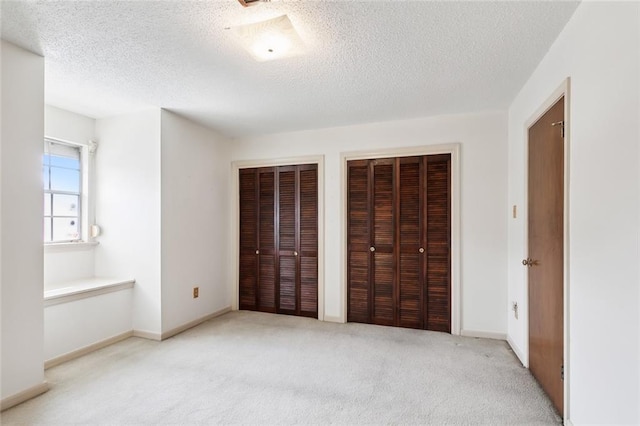 unfurnished bedroom with a textured ceiling, two closets, and light colored carpet