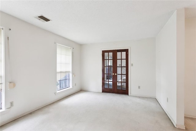 spare room with french doors, a textured ceiling, and light colored carpet