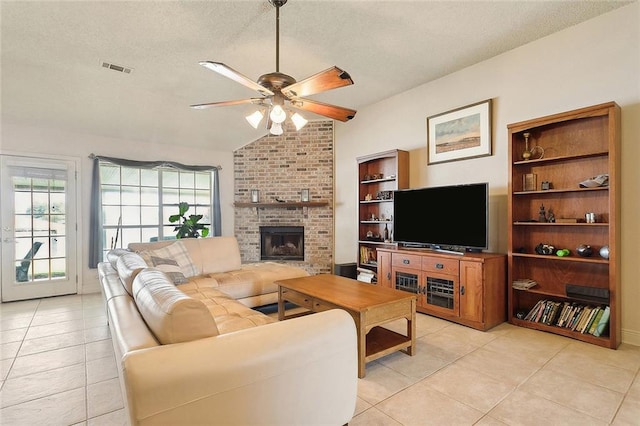 living room with a textured ceiling, light tile patterned floors, lofted ceiling, a brick fireplace, and ceiling fan