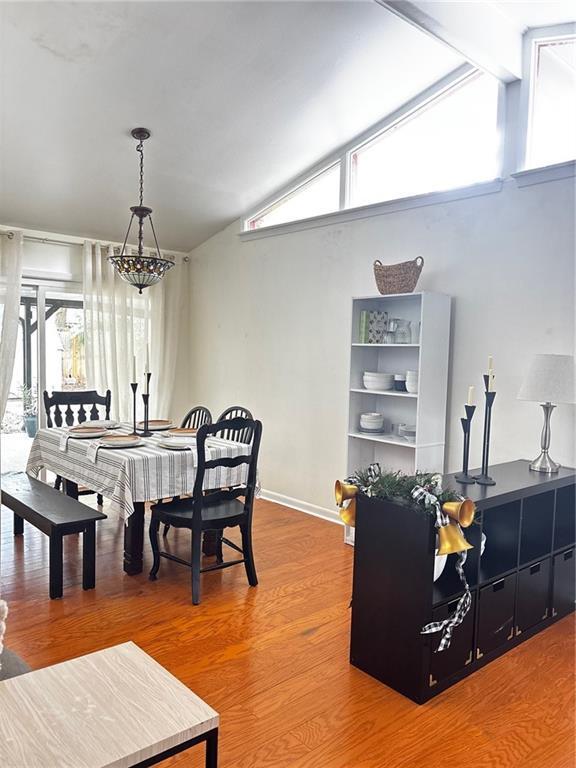 dining area with vaulted ceiling with beams, plenty of natural light, a chandelier, and hardwood / wood-style flooring