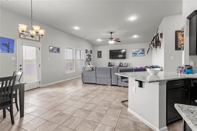 kitchen with a breakfast bar, ceiling fan with notable chandelier, light stone counters, and light tile patterned floors