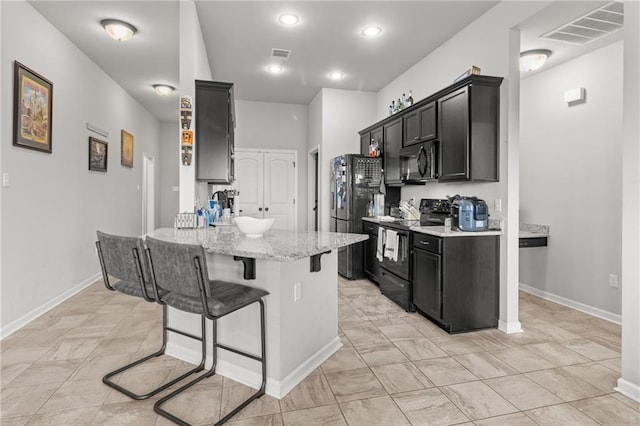 kitchen featuring light tile patterned floors, a breakfast bar area, black appliances, and light stone countertops