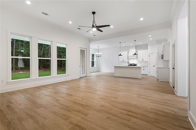 unfurnished living room featuring ceiling fan with notable chandelier, light wood-type flooring, and ornamental molding