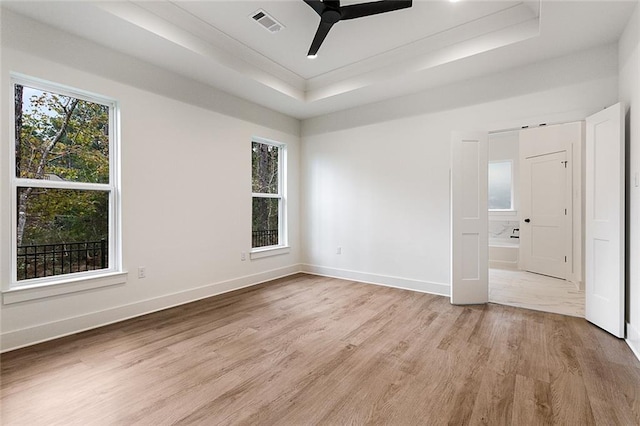 unfurnished bedroom featuring a raised ceiling, ensuite bathroom, light hardwood / wood-style flooring, and ceiling fan