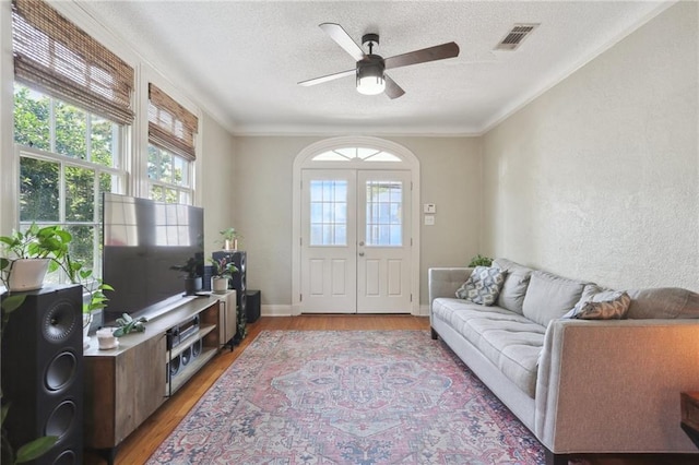 living room featuring light hardwood / wood-style flooring, a textured ceiling, ornamental molding, and ceiling fan