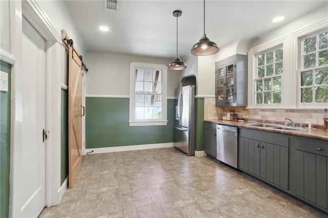 kitchen featuring appliances with stainless steel finishes, a barn door, gray cabinets, light tile patterned floors, and tasteful backsplash