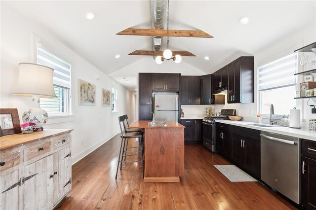 kitchen with gas stove, hardwood / wood-style floors, white refrigerator, stainless steel dishwasher, and vaulted ceiling with beams