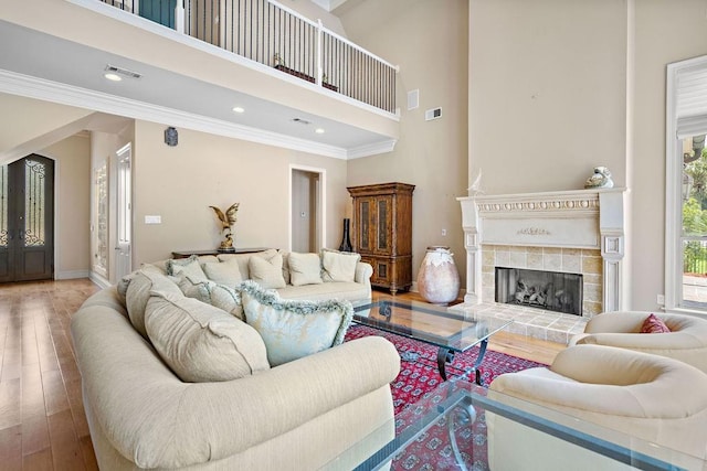 living room with hardwood / wood-style floors, a towering ceiling, crown molding, and a tile fireplace