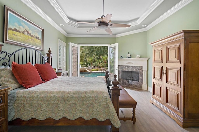 bedroom with ornamental molding, light wood-style flooring, a fireplace, a raised ceiling, and access to outside