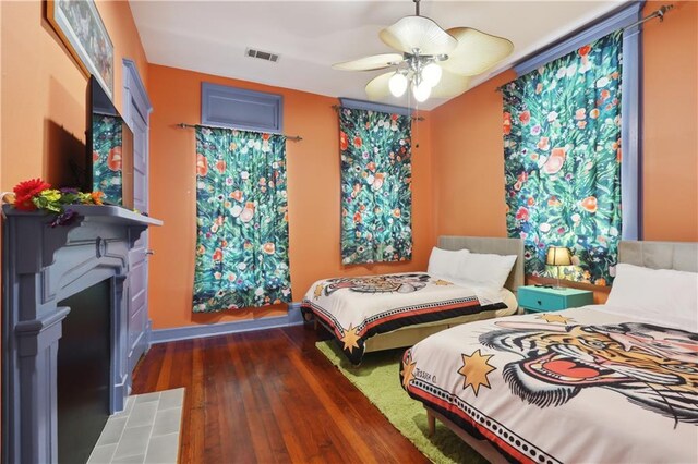 bedroom with a tiled fireplace, dark wood-type flooring, and ceiling fan