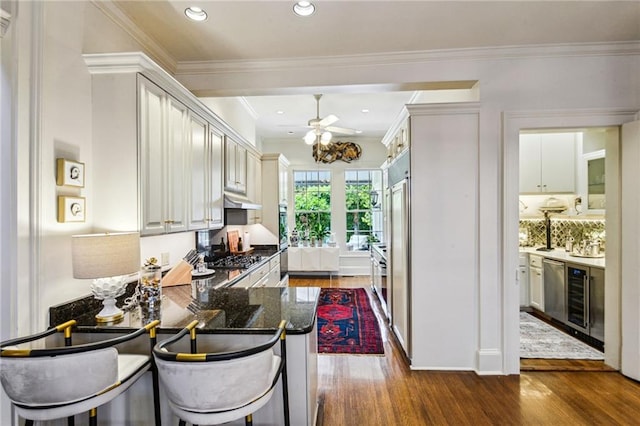 kitchen with kitchen peninsula, a kitchen bar, crown molding, and dark wood-type flooring