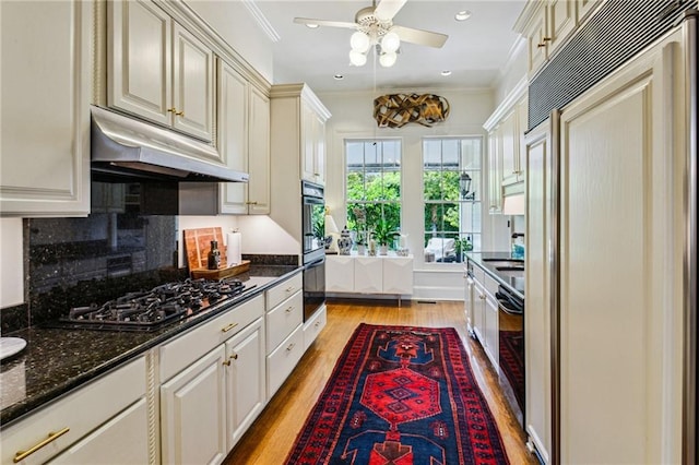 kitchen featuring appliances with stainless steel finishes, ornamental molding, cream cabinets, light hardwood / wood-style flooring, and dark stone countertops