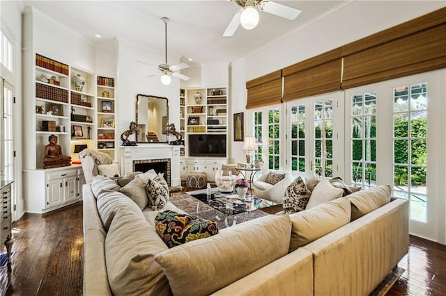 living room with ceiling fan, dark wood-type flooring, built in features, a fireplace, and ornamental molding