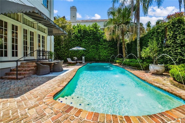 view of swimming pool with pool water feature, french doors, and a patio