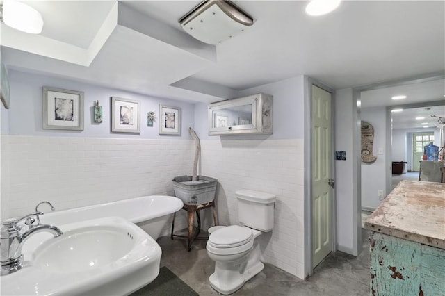 bathroom featuring concrete flooring, a bathing tub, vanity, tile walls, and toilet